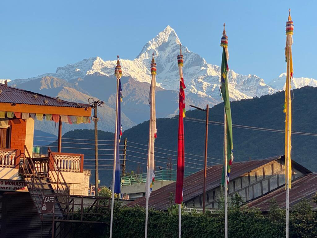 Colorful prayer flags flying above traditional Tibetan houses with snow-capped Annapurna and Fishtail mountains in the background