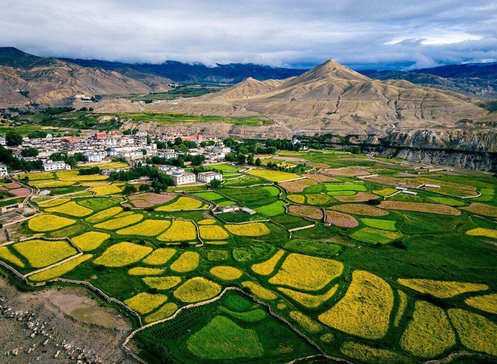 Panoramic view of Lo Manthang village with traditional houses, surrounding hills, and green farmland in the high Himalayas.