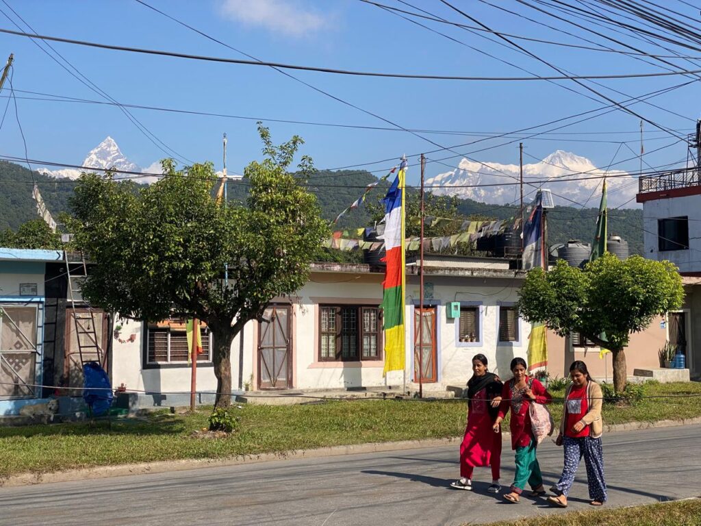 Tibetan refugee settlement in Nepal with village houses, prayer flags, and Annapurna mountain views