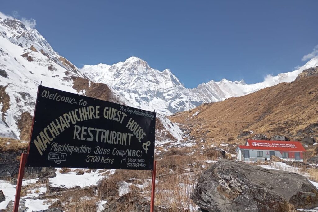 Machhapuchhre Base Camp MBC sign at 3700m with the Annapurna Rescue Center and snowy mountain peaks.