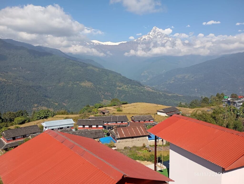Red corrugated rooftops of a Nepali village with Machhapuchhre Fishtail mountain rising above white clouds