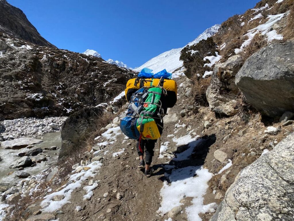 Nepali porter carrying heavy load along the rocky Dudh Koshi River trail Everest region Nepal