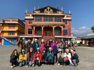 Group of travellers on a Pokhara cultural tour posing in front of a colourful Tibetan Buddhist monastery with Himalayan peaks in the background