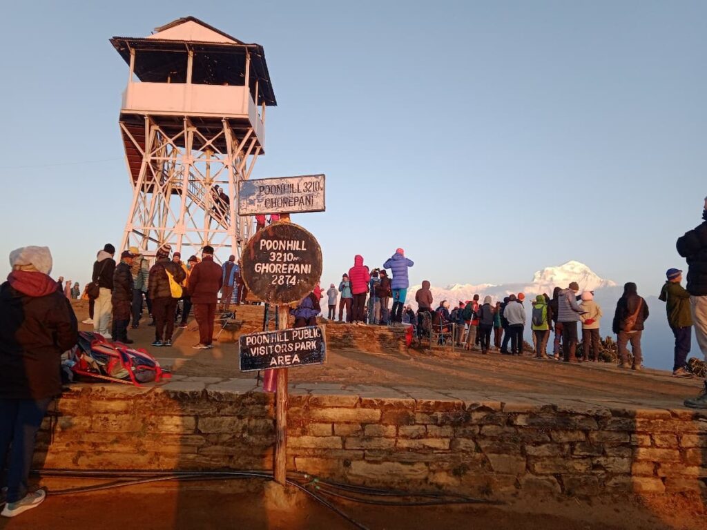 Crowds of trekkers gathered at Poon Hill summit signboard at 3210m during sunrise with Dhaulagiri mountain view on the Ghorepani Poon Hill Trek Nepal