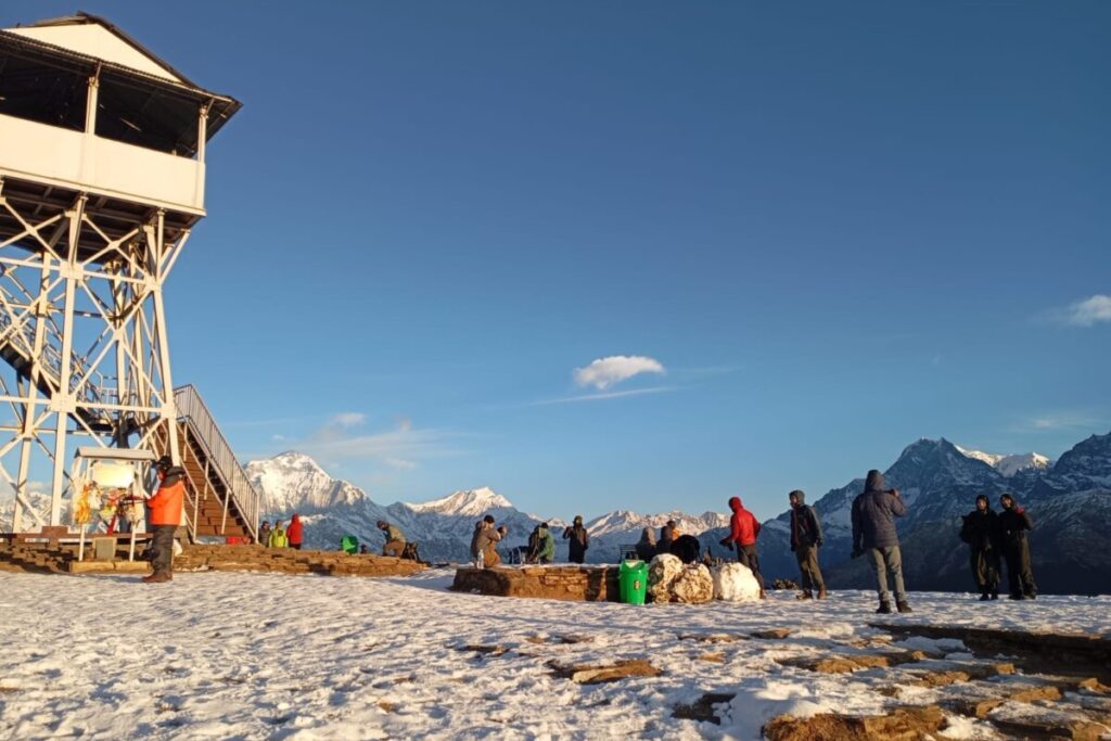Trekkers gathering at the Poon Hill viewpoint tower at sunrise with snowy Annapurna peaks in the background.