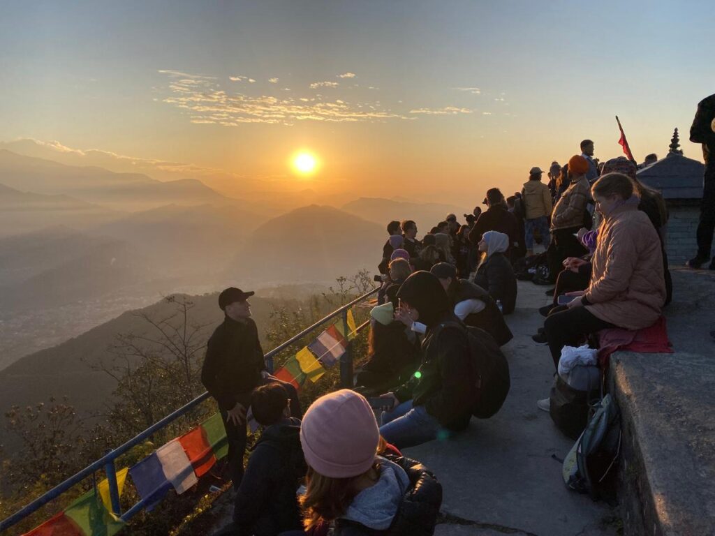 Travellers gathered at Sarangkot viewpoint
watching the golden sunrise over the misty
valley with colorful Buddhist prayer flags