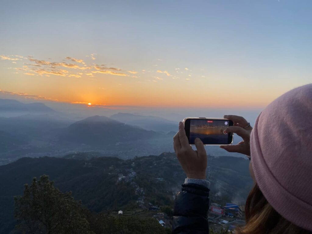 A traveller photographing the breathtaking
orange sunrise and misty valley views from
Sarangkot viewpoint near Pokhara