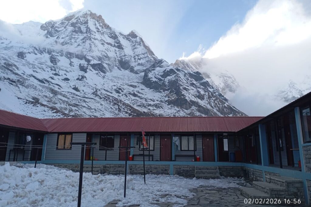 Snow-covered courtyard of a traditional tea house with Annapurna South peak in the background at Annapurna Base Camp.