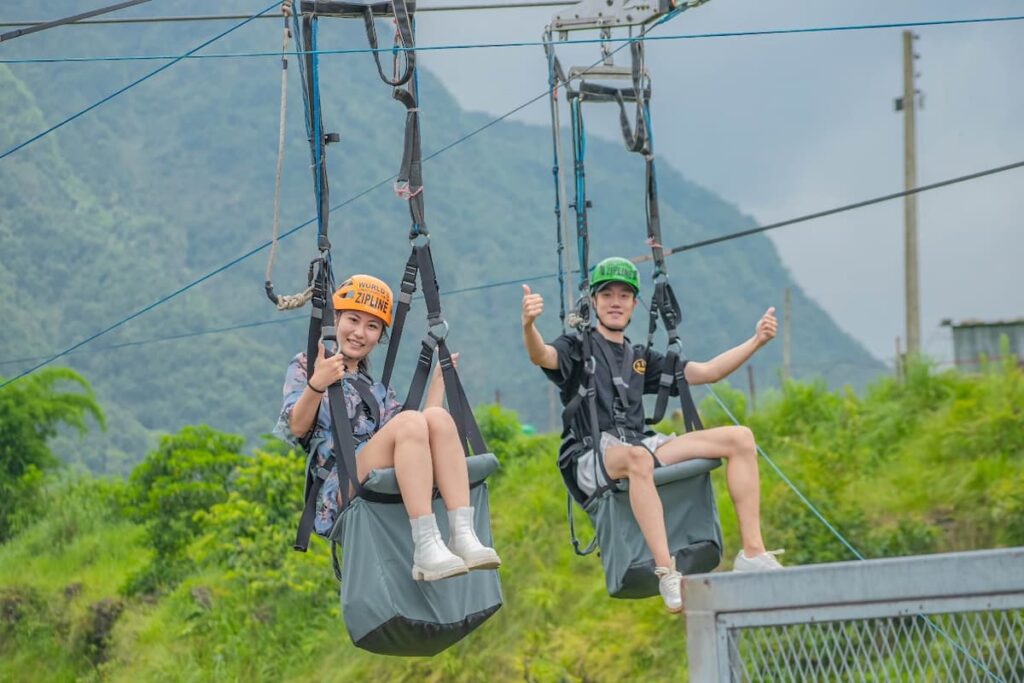 Two guests ziplining side by side above green hills near Pokhara Nepal.