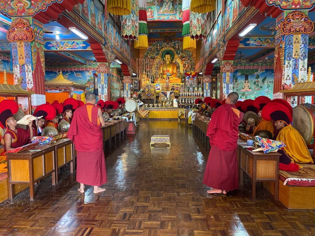 Monks in red robes performing group prayer chanting inside an ornate Tibetan Buddhist monastery during an afternoon visit in Pokhara