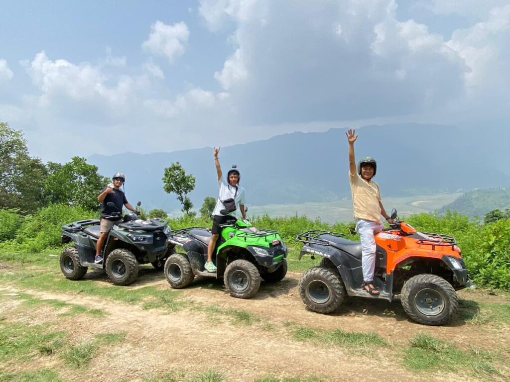 Three guests riding ATV quad bikes on a hilltop trail with Annapurna mountain views