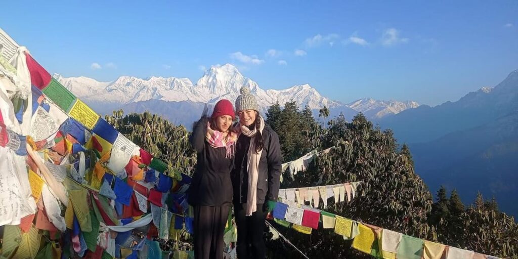 Two hikers with colorful prayer flags and Annapurna mountain view at Australian Camp on a Dhampus hike