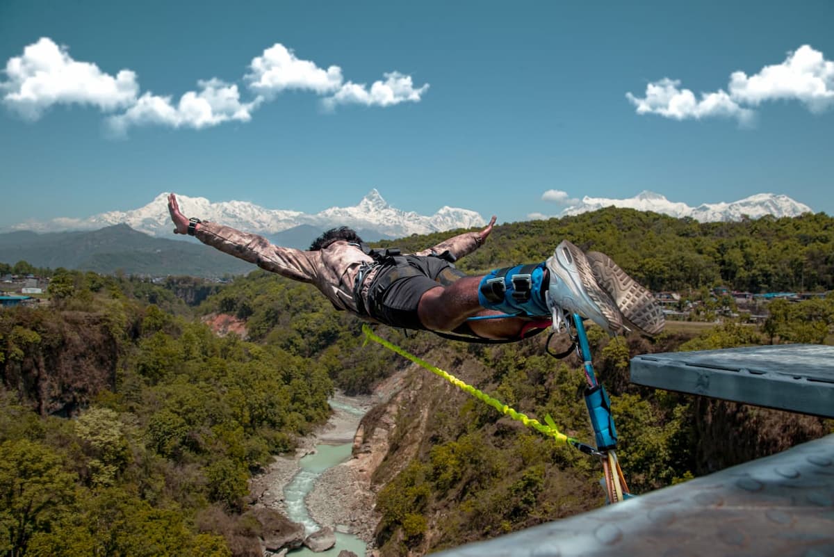 Person bungee jumping over the Seti River gorge with snow-capped Annapurna mountains in the background