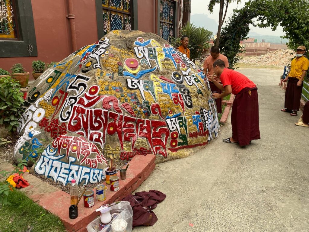 Buddhist monks carefully painting colourful sacred Tibetan mantras onto a large stone at a monastery in Pokhara