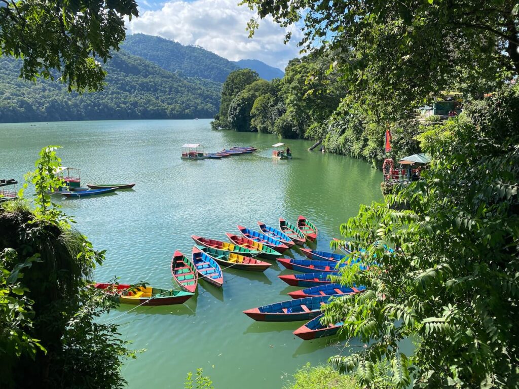 Colourful wooden boats moored on the calm green waters of Phewa Lake with mountain reflections