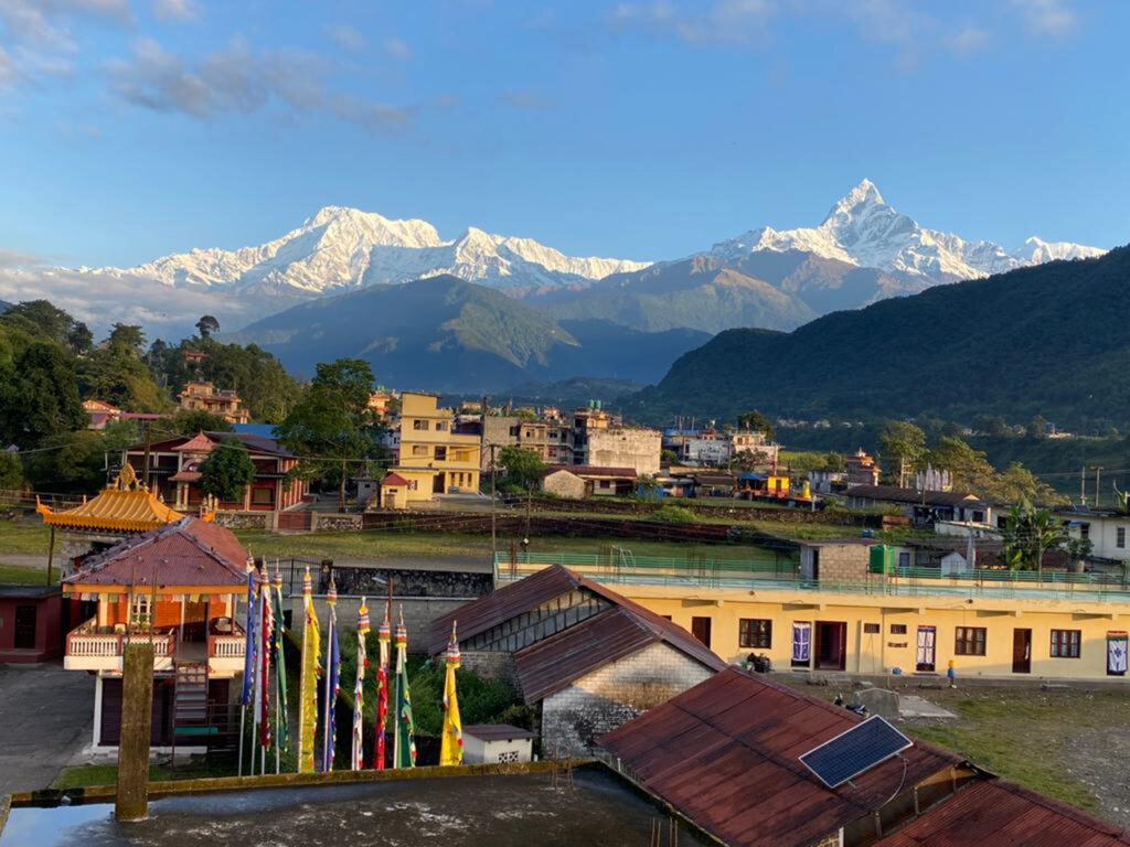 Aerial view of a Tibetan refugee settlement with rows of traditional buildings and Annapurna and Machhapuchhre peaks in the distance