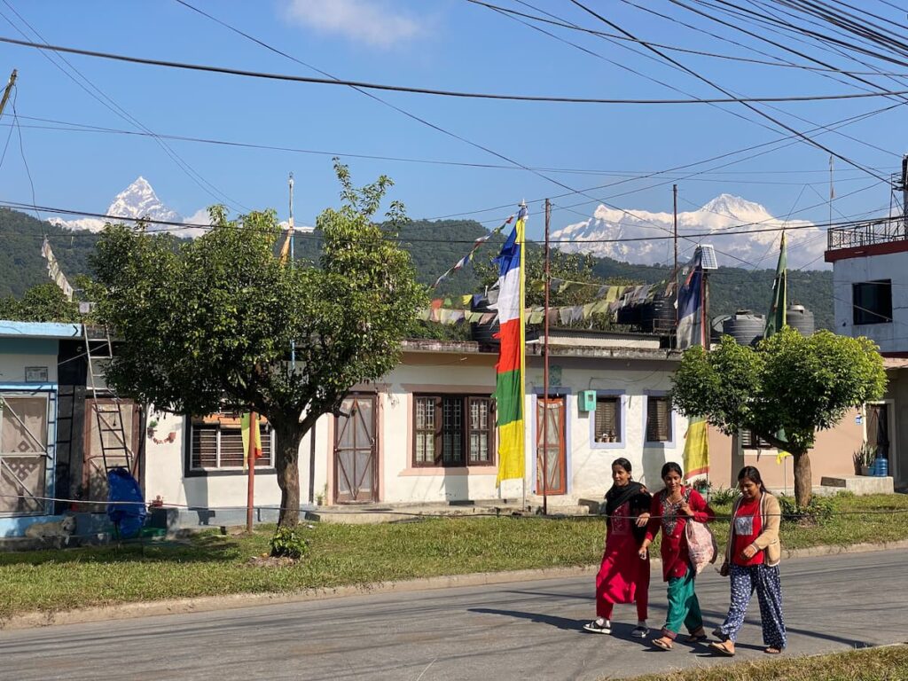 Local women walking past traditional houses decorated with Buddhist prayer flags with Fishtail mountain in the background