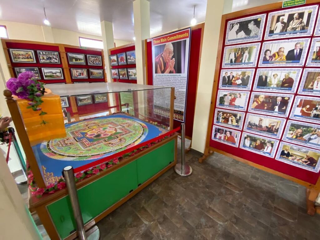 A sand mandala displayed alongside historical photographs inside a community gallery