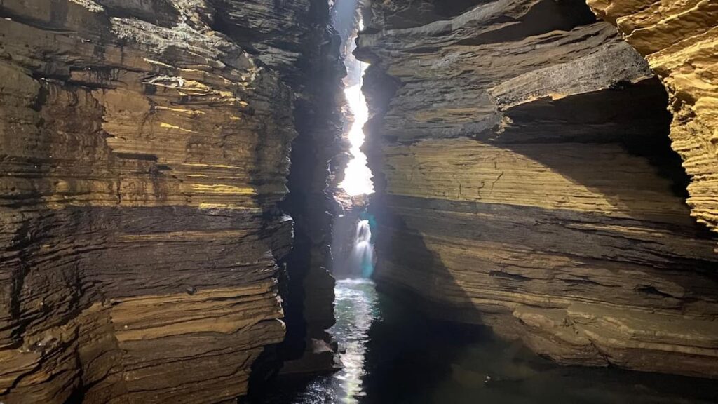 Underground waterfall inside Gupteshwor Mahadev Cave in Pokhara with natural light streaming through a narrow rock opening above