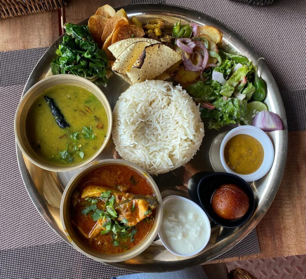 Traditional Nepali dal bhat set meal served on a steel plate with rice, lentil soup, vegetable curry and pickle.