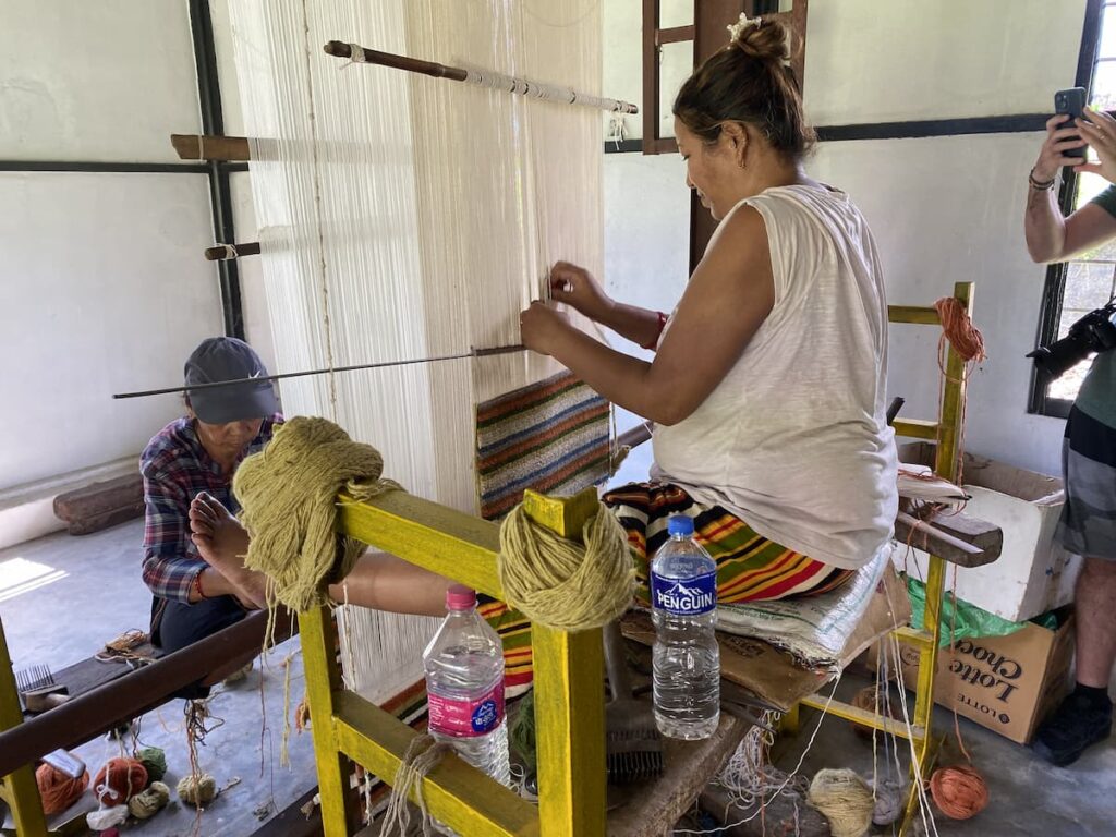 Tibetan women demonstrating traditional carpet weaving at the refugee settlement — a cultural highlight on the Pokhara sightseeing by car tour.