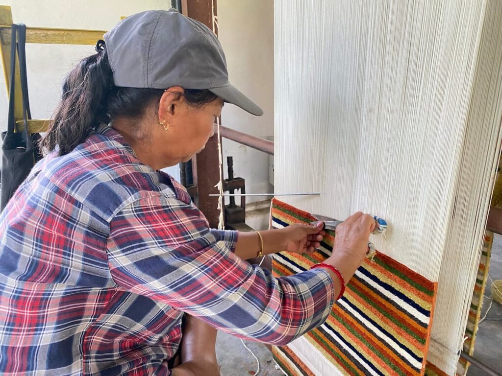 A Tibetan woman weaving a traditional striped carpet on a hand loom at the Tibetan Refugee Settlement in Pokhara.