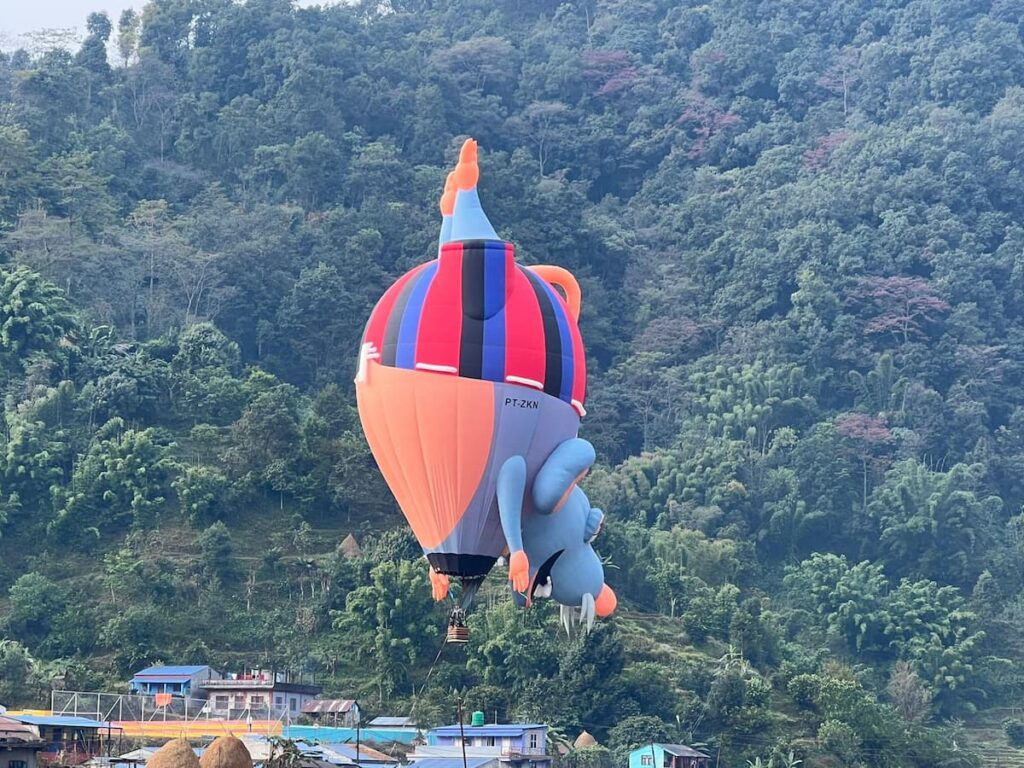 Hot air balloon Nepal novelty-shaped balloon flying over a green forested hillside