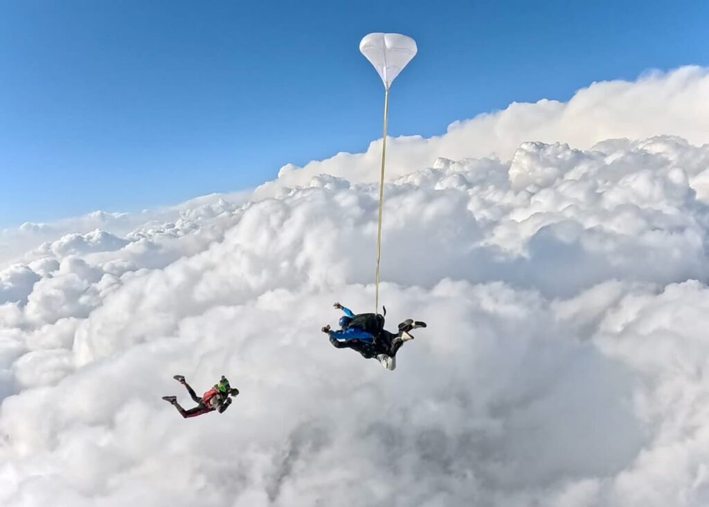 An open white parachute canopy floating above a sea of clouds