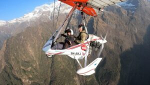 Pilot and passenger in an open ultralight aircraft above Pokhara's forested hills