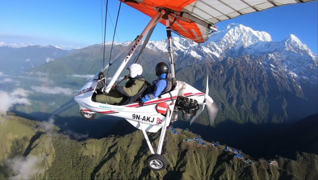 Open ultralight aircraft flying over Pokhara Valley with the Annapurna range behind